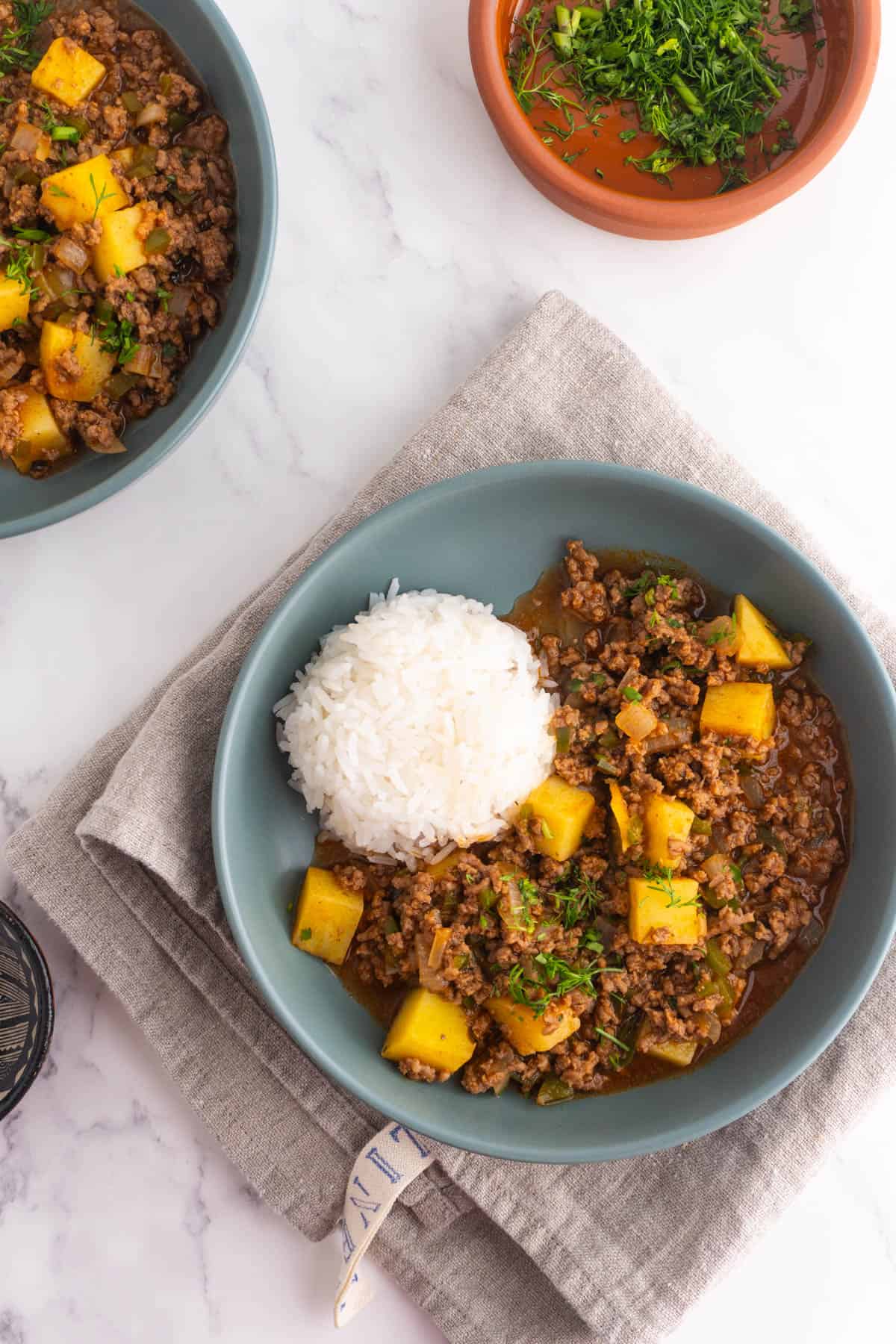 Shallow bowl served with ground beef picadillo and potatoes with rice on the side.