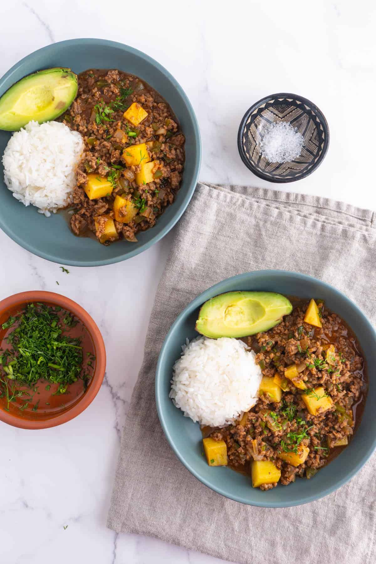 Two shallow bowls of Mexican picadillo served with rice and a side of avocado.