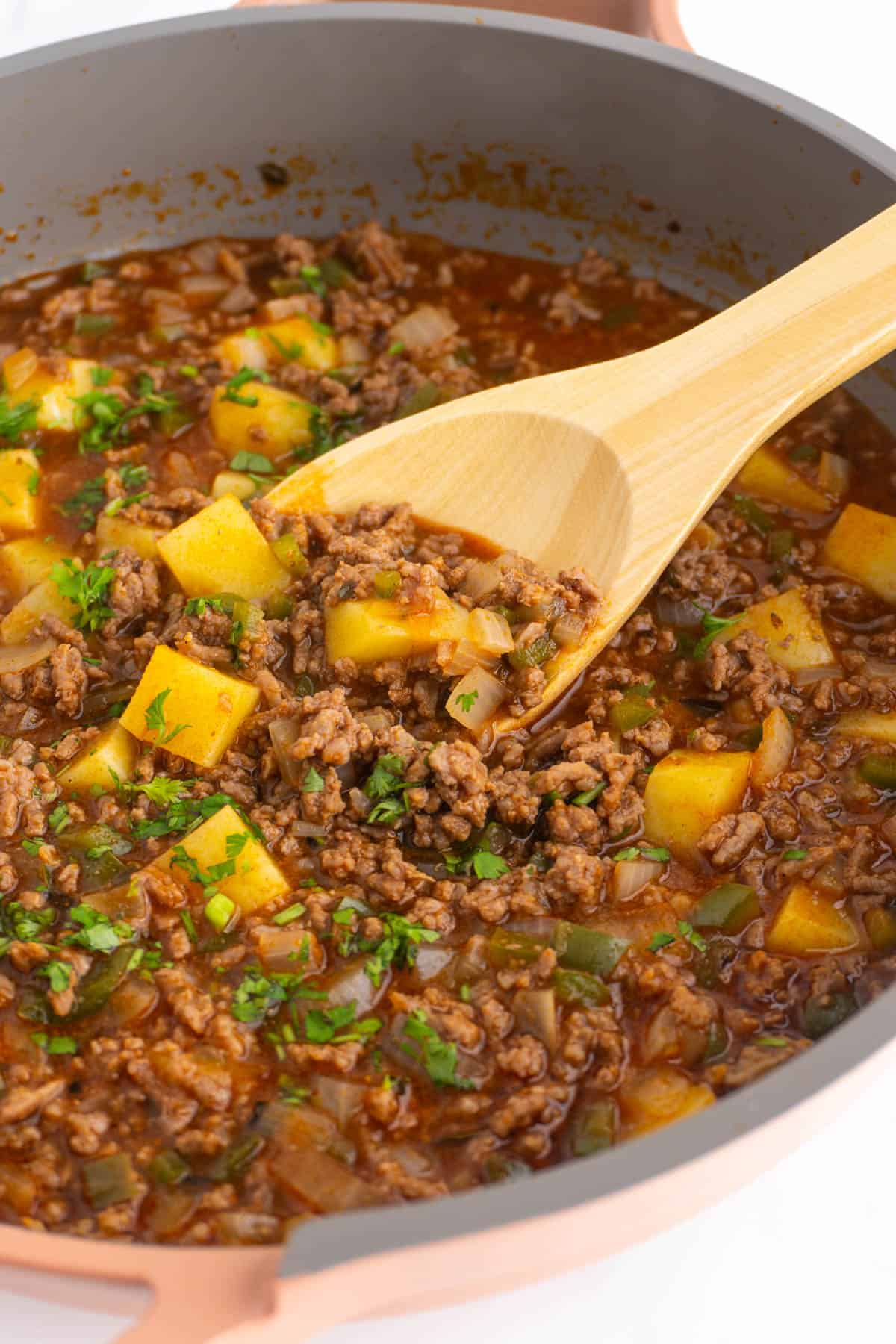 Mexican picadillo in a skillet with a wooden spoon.