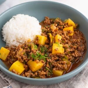 Mexican picadillo in a blue shallow bowl with a side of rice.