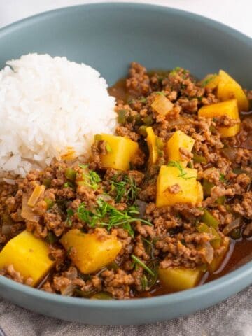 Mexican picadillo in a blue shallow bowl with a side of rice.