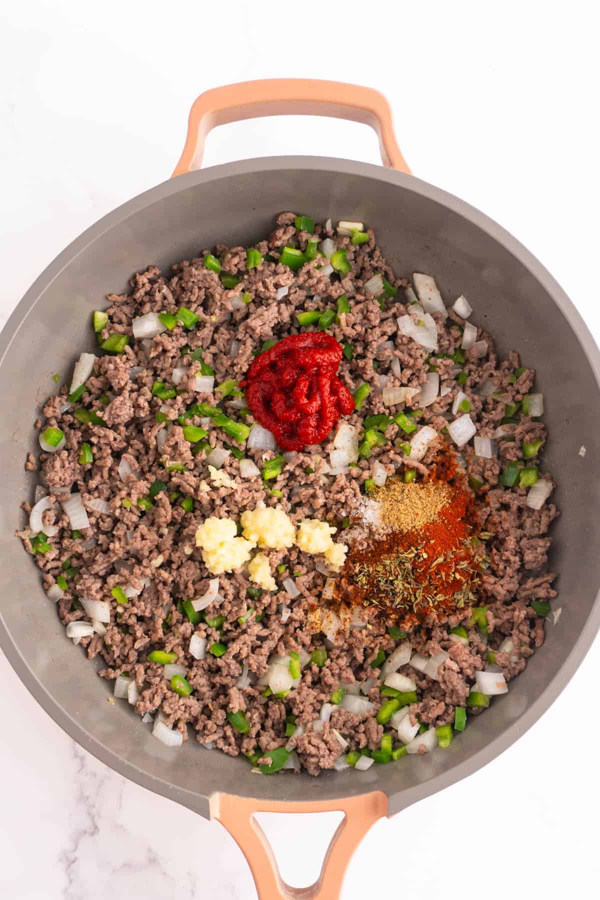 Ground beef mixture in a skillet topped with spices, garlic and tomato paste before being mixed.