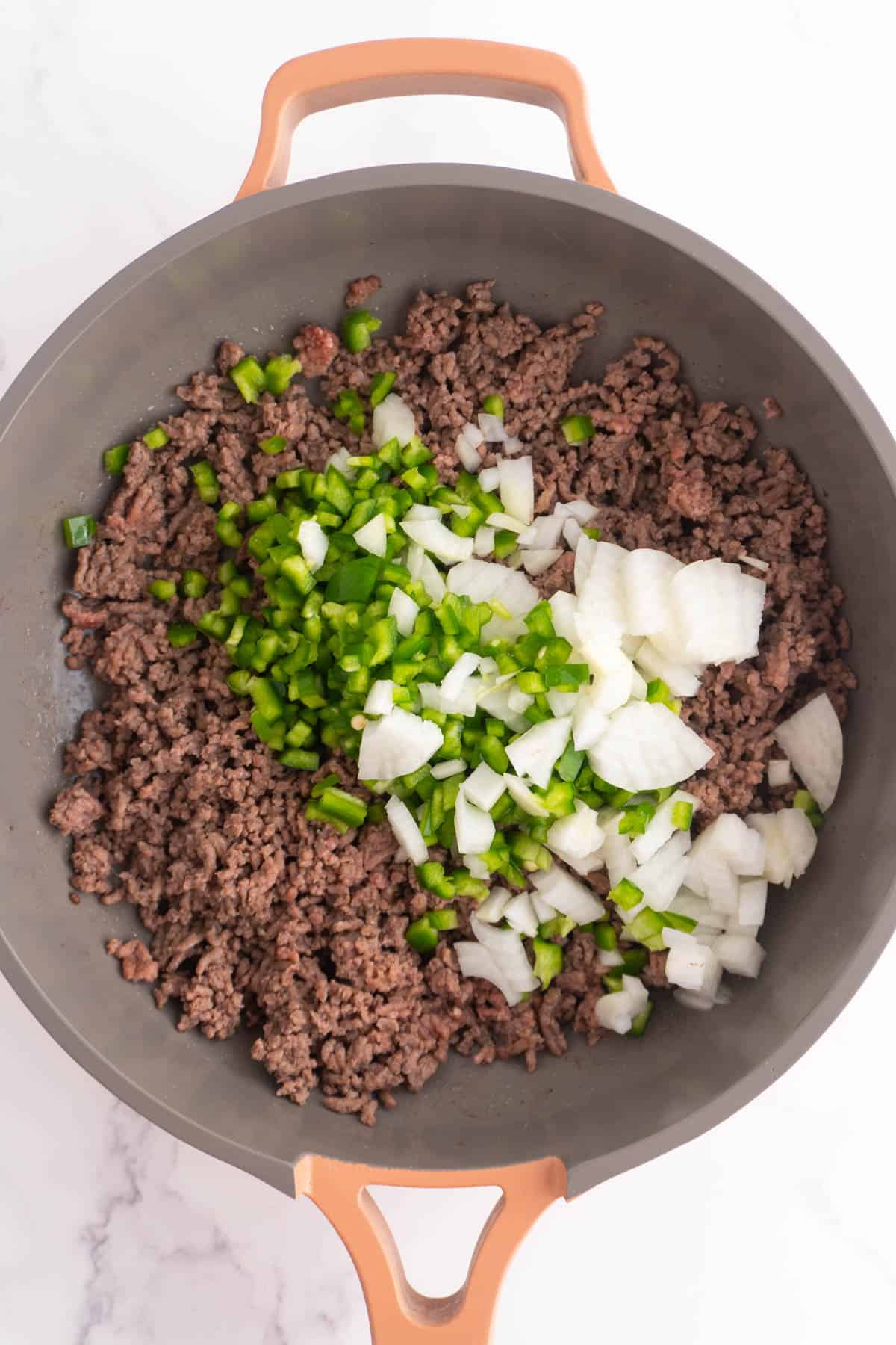 Diced green peppers and onions added to the ground beef in a skillet.