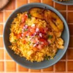 Arroz con camarones in a bowl with sweet plantains and tomato onion salad on top.