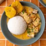Fish in coconut sauce served with a side of rice and fried plantains.