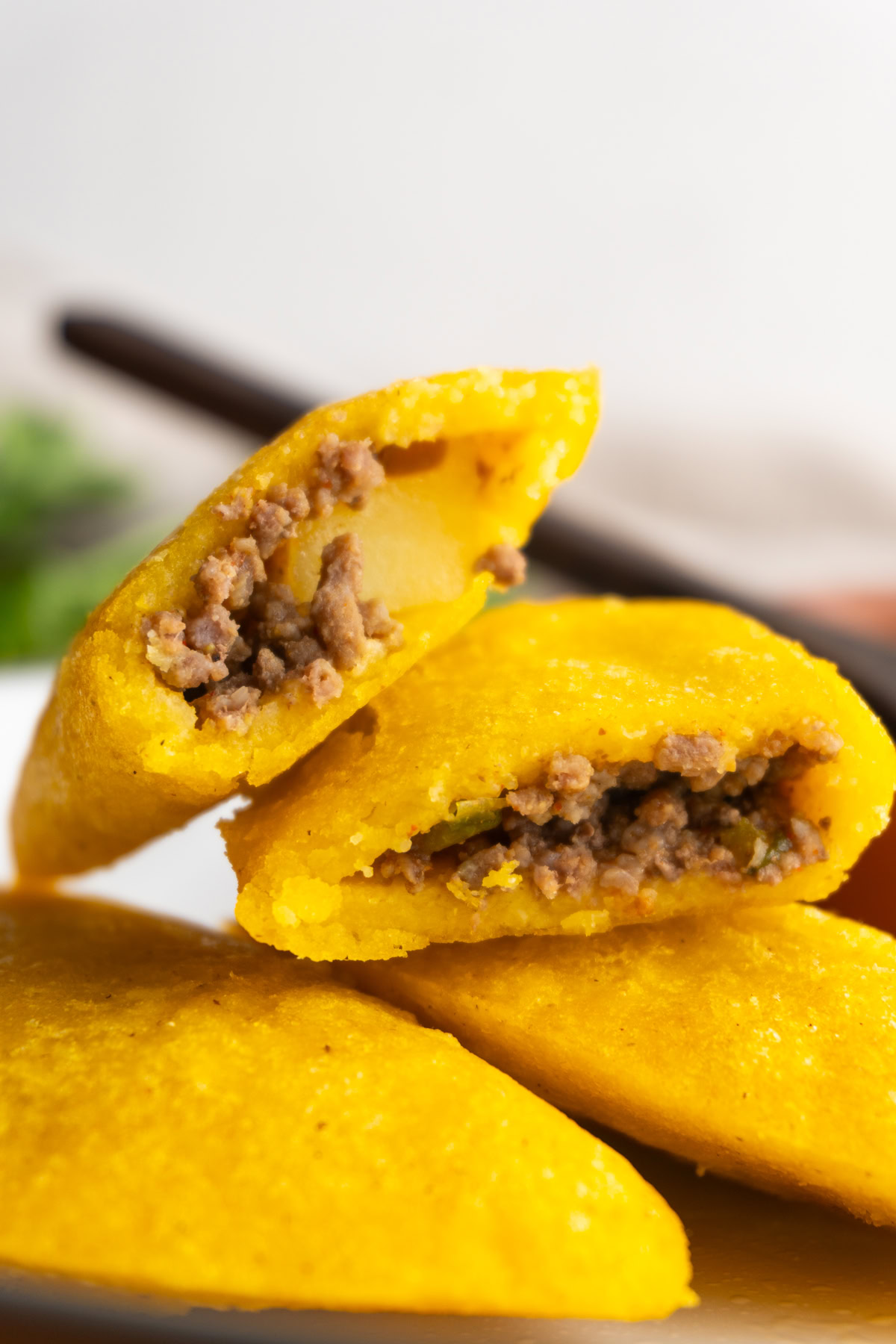 Two Colombian empandas on a plate with one cut in half on top of them showing the inside.