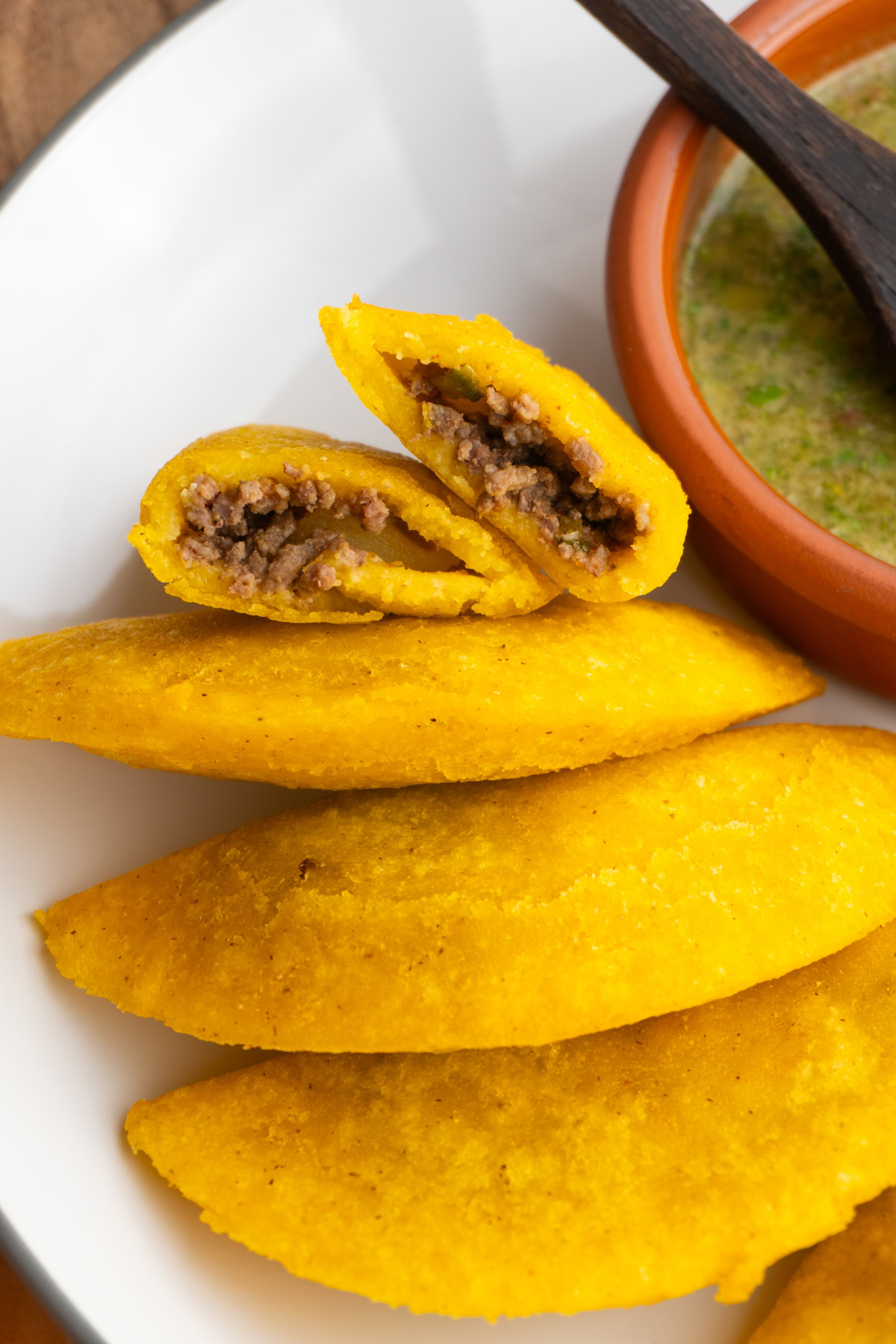 Overhead shot of Colombian empanadas on a plate with one cut in half to show the filling.