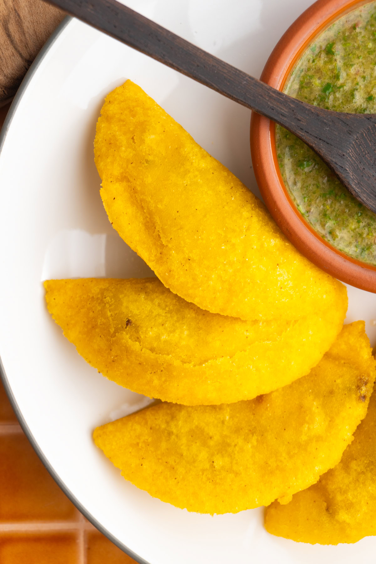 Close up of Colombian empanadas on a white plate next to a small bowl of ají.