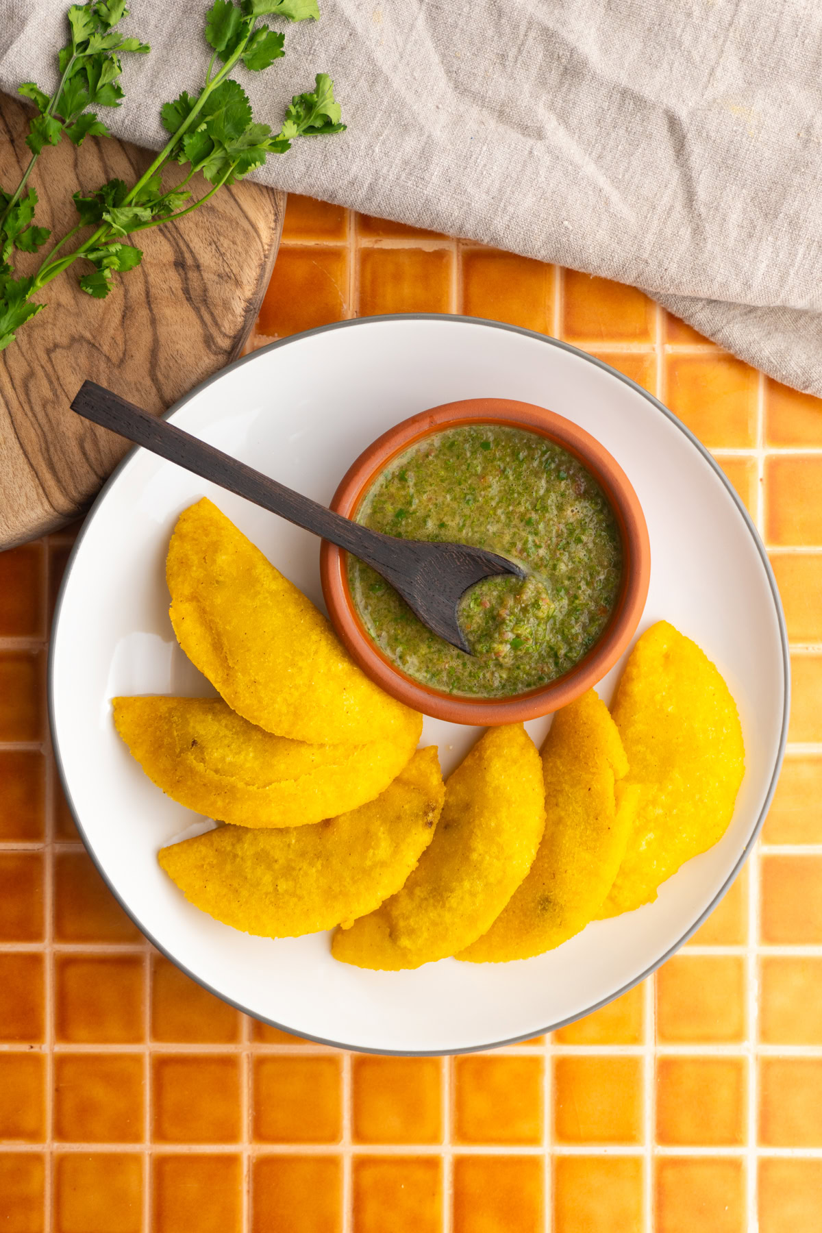 Overhead shot of Colombian empanadas on a white plate with a bowl of Colombian ají.