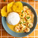 Encocado de camarón served in a bowl with rice and a side of plantains.