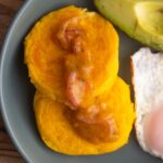 Close up of two llapingacho potato patties with hot sauce on top.
