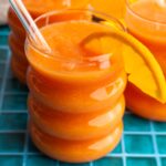 Papaya mango smoothie in a bubble glass with a straw and slice of orange.