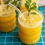 Glass of passion fruit juice garnished with mint with more glasses of juice behind it.