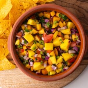 Peach mango salsa in a bowl on a wooden board served with chips.