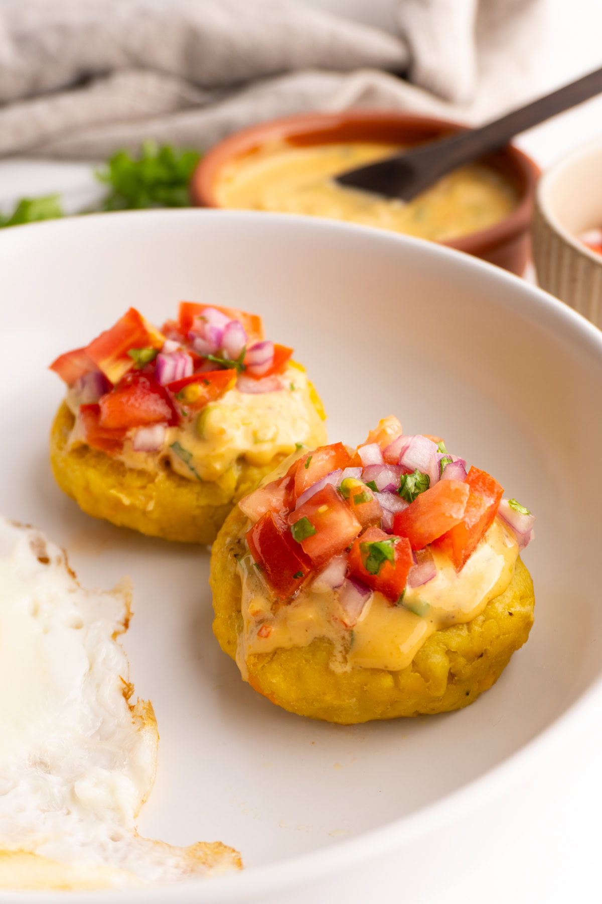 Side view of two tortillas de verde topped with peanut sauce and tomato and onions curtido.