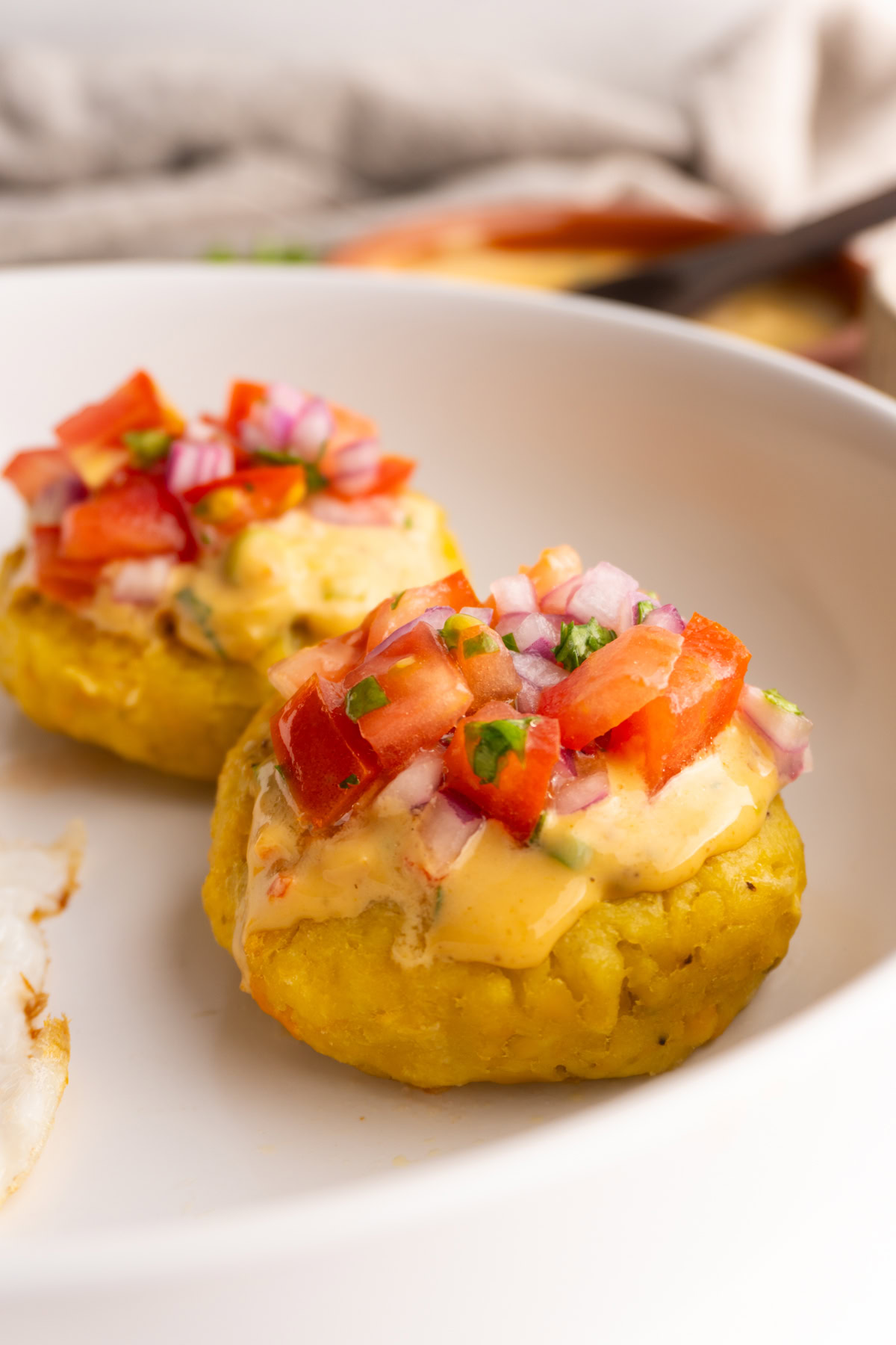 Side view of a tortilla de verde topped with peanut sauce and tomato and onion salad.
