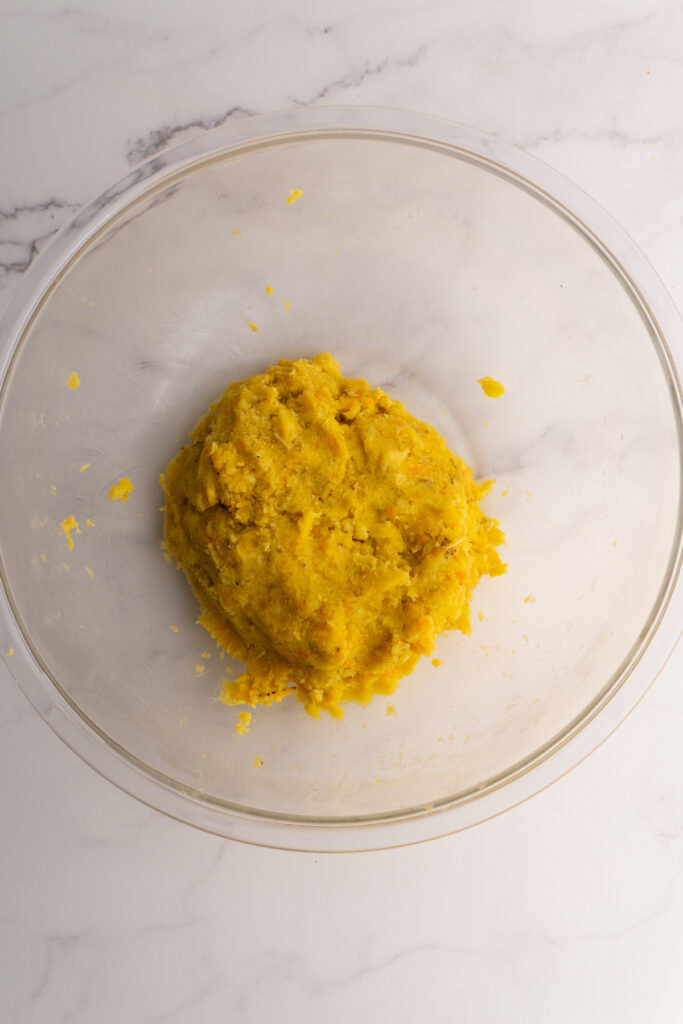 Mashed green plantain dough in a large glass bowl.