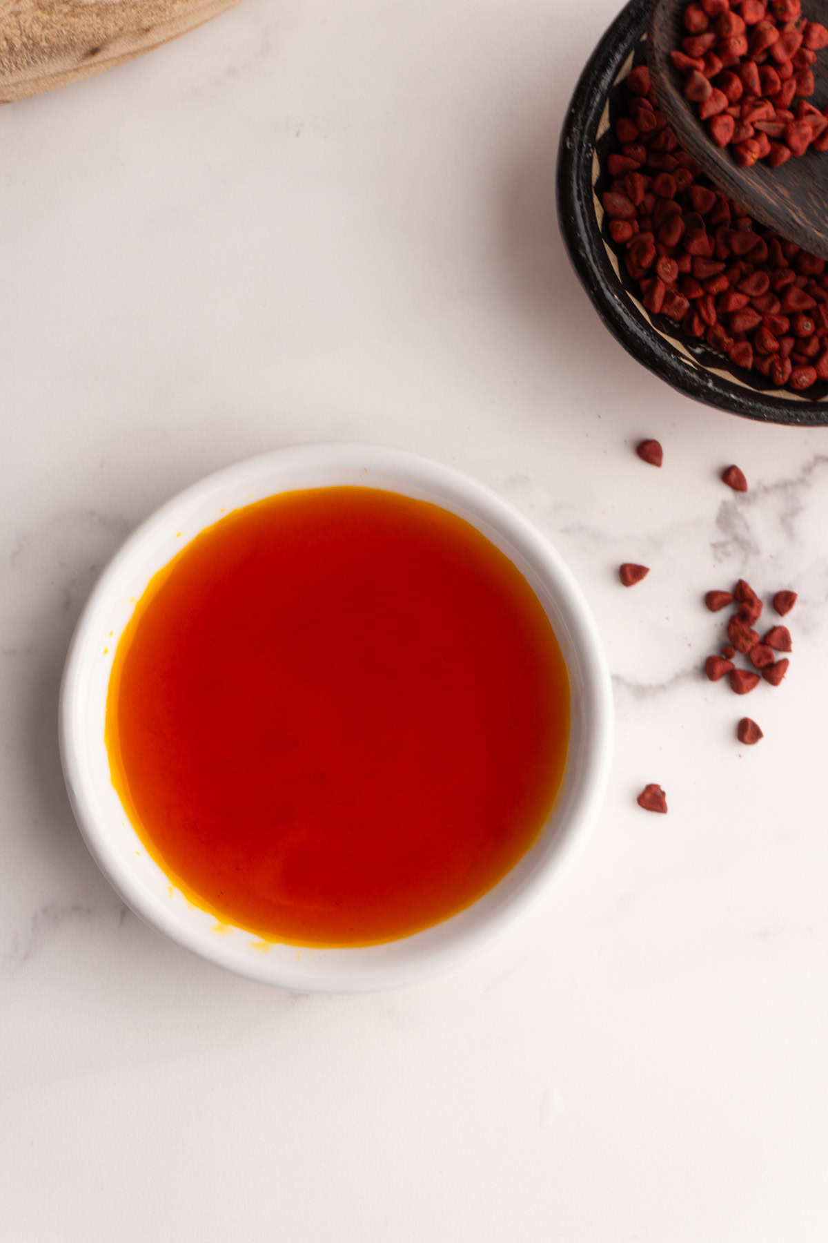 Achiote oil in a small white ramekin next to some whole annatto seeds.