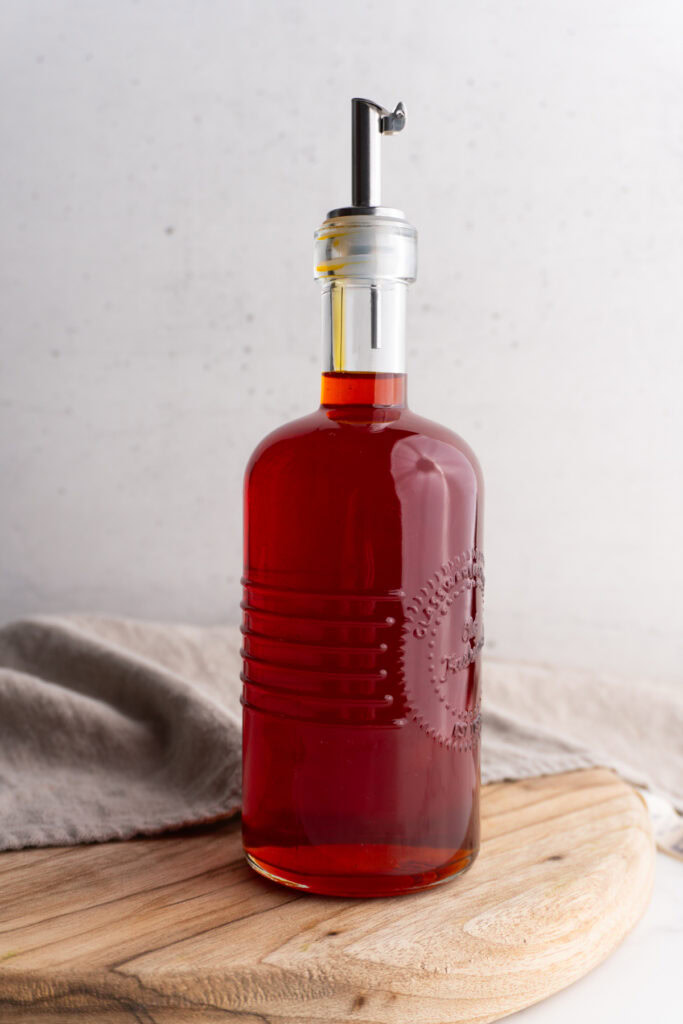 Side view of achiote oil in an oil dispenser on a wooden board.