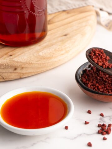 Achiote oil in a small ramekin next to whole annatto seeds.