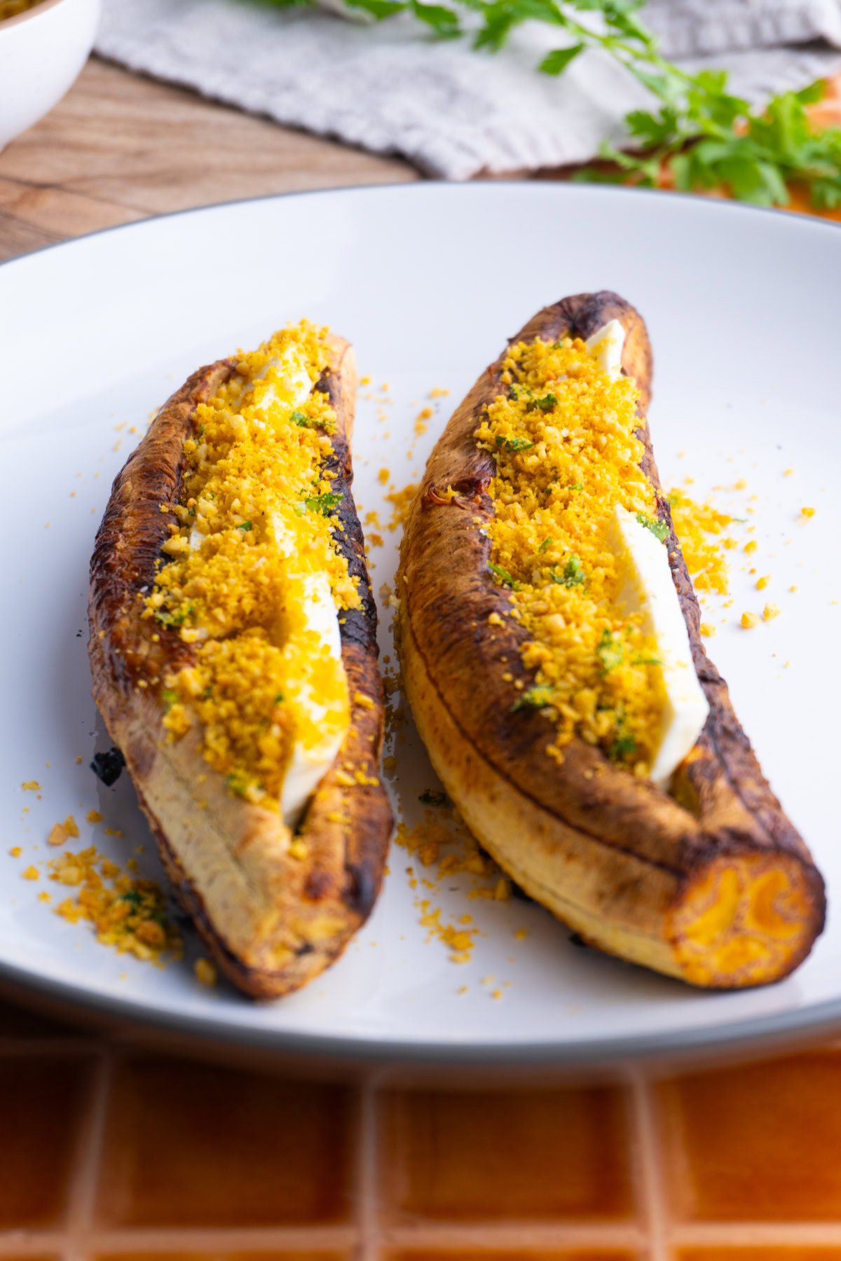 Side view of two baked plantains with cheese and salprieta on a white plate.