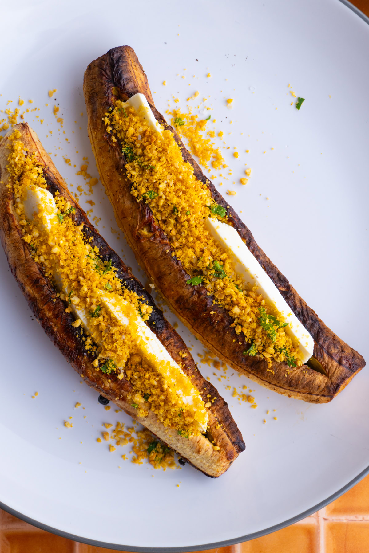 Two baked plantains with cheese on a white plate, garnished with salprieta.