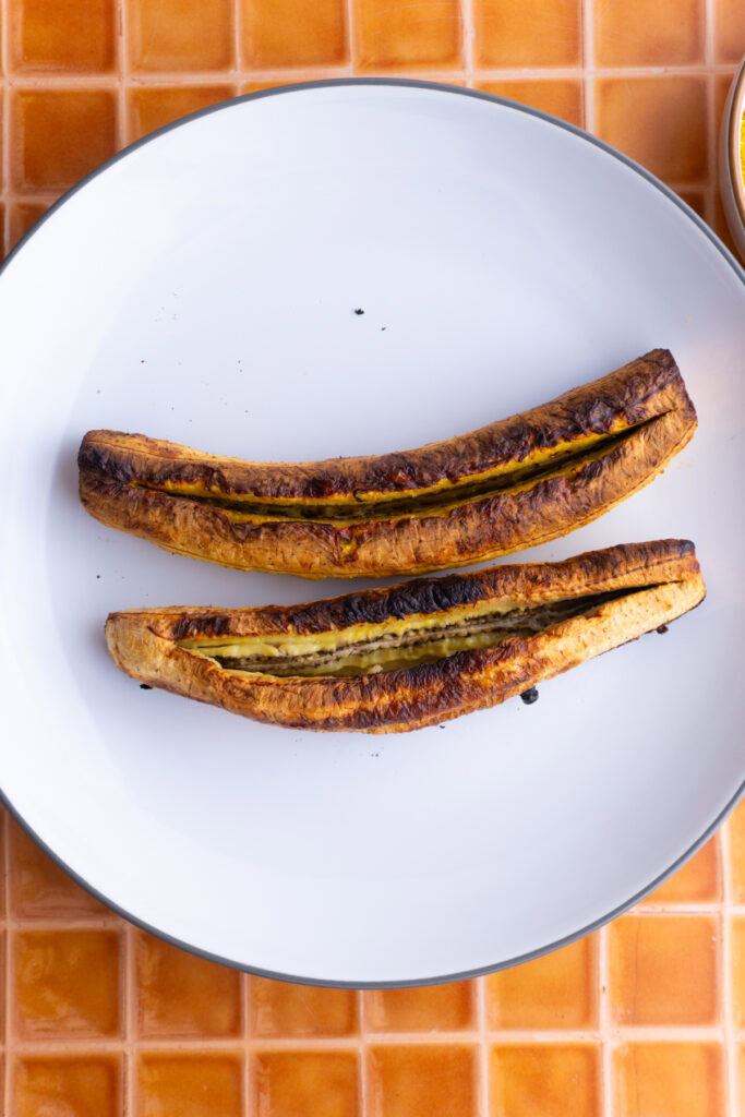 Two baked plantains with a slice made on the top of each.