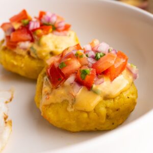 Side view of two tortillas de verde topped with peanut sauce and tomato onion curtido.