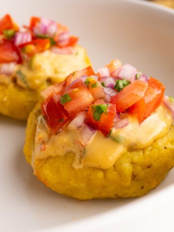 Side view of two tortillas de verde topped with peanut sauce and tomato onion curtido.