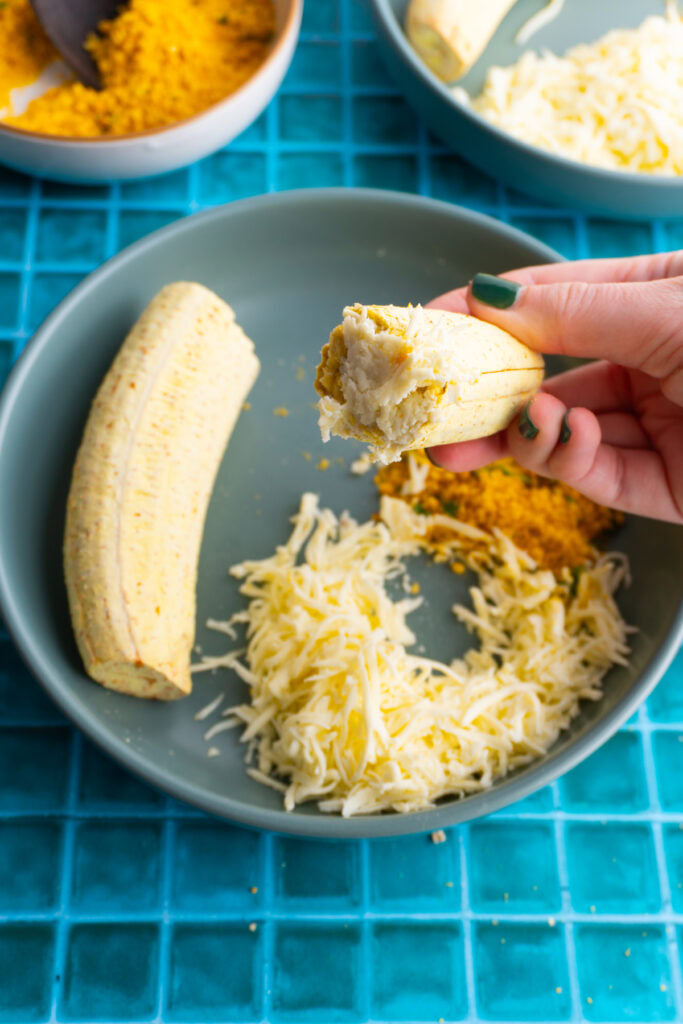 Hand holding a piece of roasted plantain dipped in cheese.