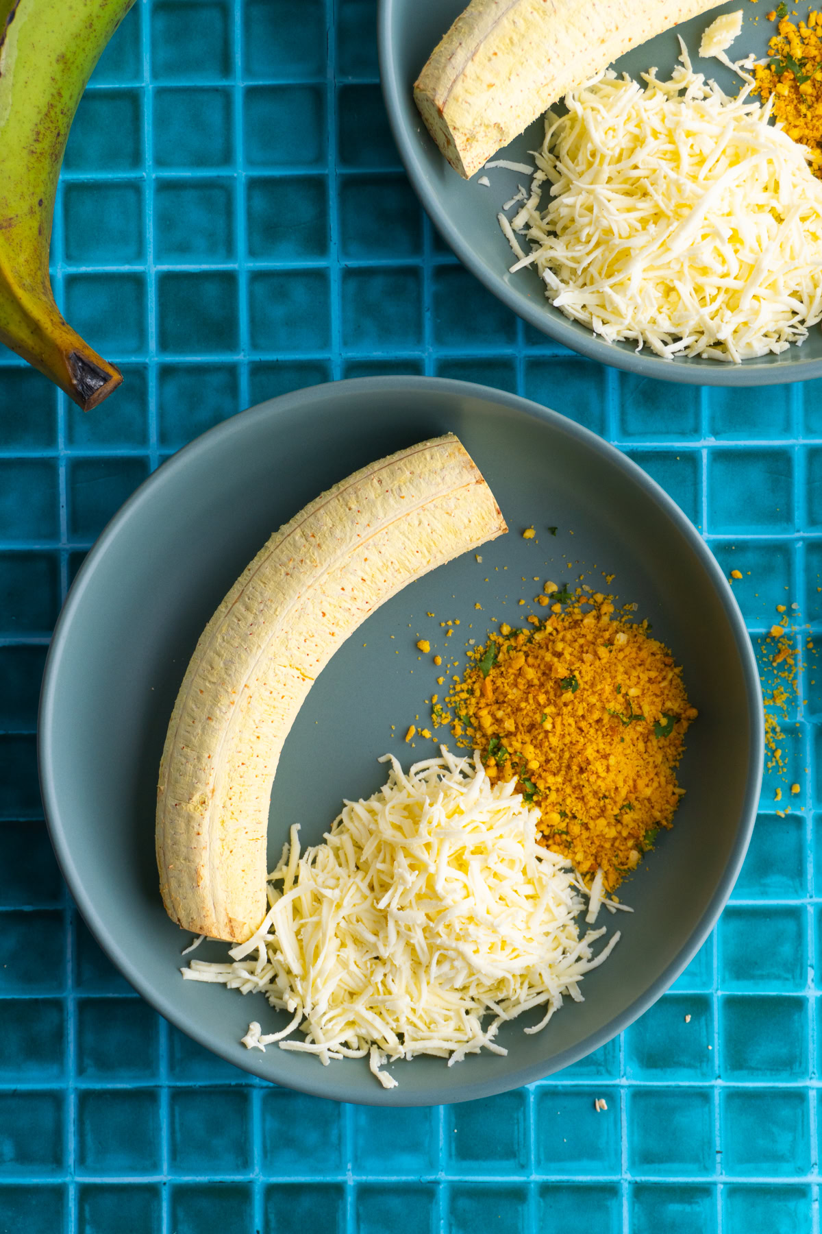 Roasted green plantain in a shallow bowl with shredded cheese and salprieta.