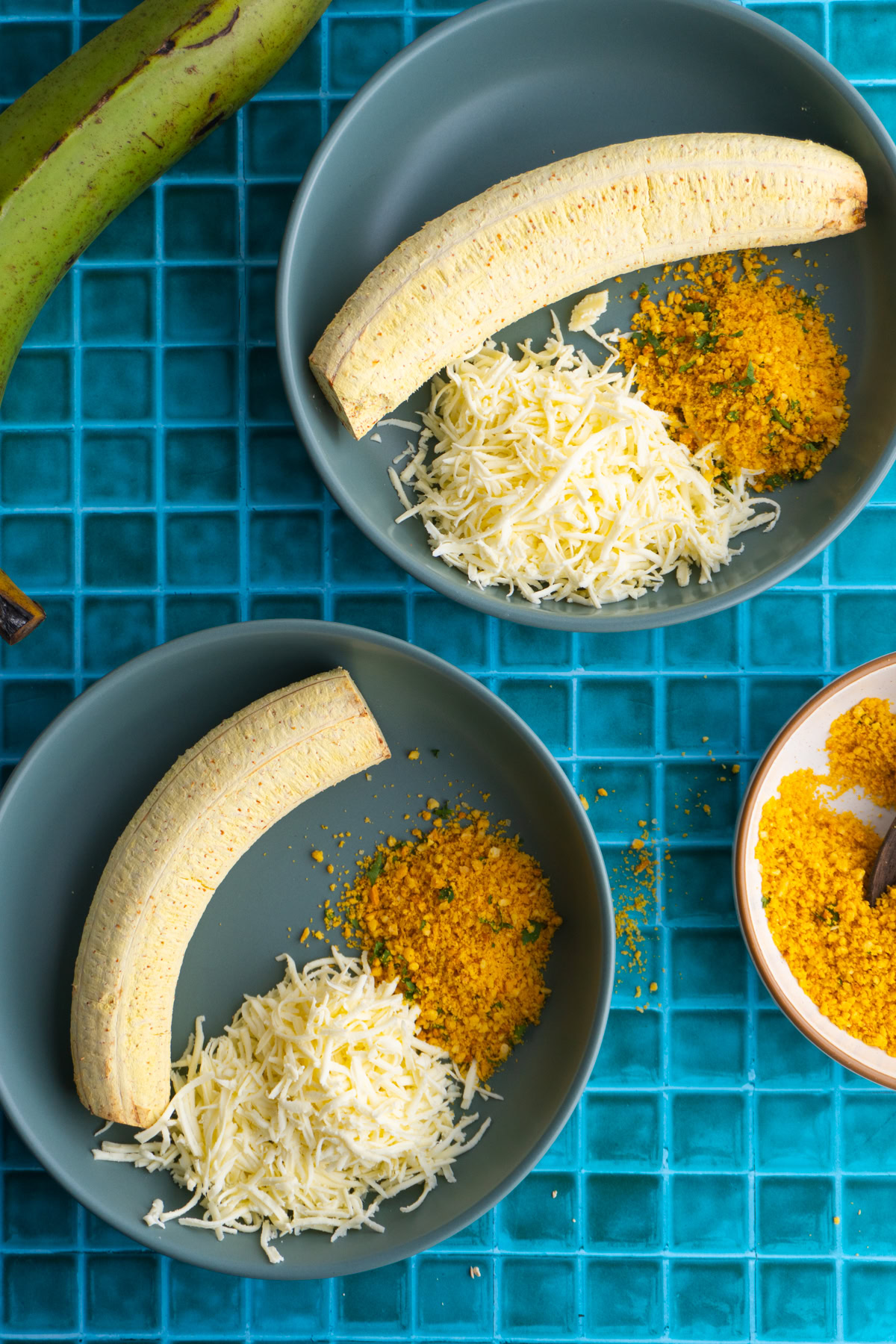 Two green plantains with shredded cheese and saplrieta on the side.