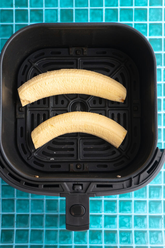 Two green plantains in an air fryer before cooking.